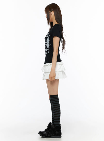 Graphic U-Neck Tee IL523 Black side view on model showing slim fit silhouette, short cap sleeves, and graphic print partially visible, white layered skirt styling