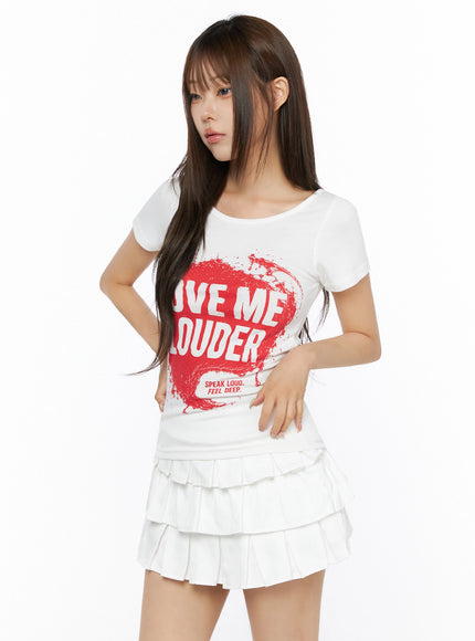 Graphic U-Neck Tee IL523 White three-quarter front view on model with red LOVE ME LOUDER splash print, paired with white tiered pleated mini skirt