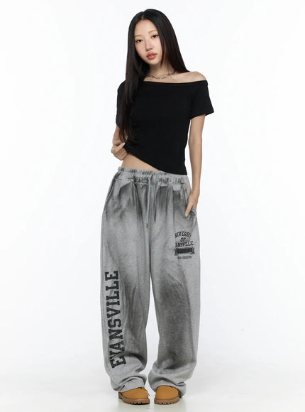 Graphic Wide Leg Sweatpants CL527 Gray front full-length shot on model in black off-shoulder top hands in pockets collegiate logo print visible