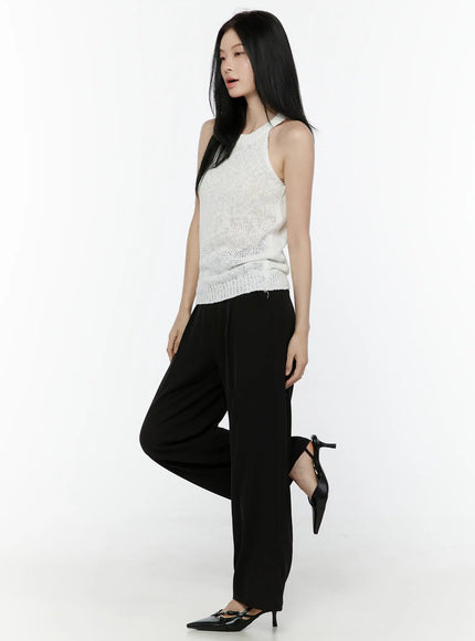 Halter Knit Top IL506 White side dynamic shot on model one leg raised showing halter neckline open knit semi-sheer body with ribbed hem and black trousers