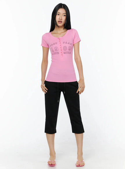 Henley Graphic Tee IL509 Pink front full-body shot model standing arms at sides styled with black cropped drawstring pants and pink sandals