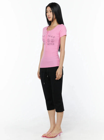 Henley Graphic Tee IL509 Pink three-quarter side shot model standing slightly turned showing fitted ribbed silhouette and short sleeve detail with black capri pants