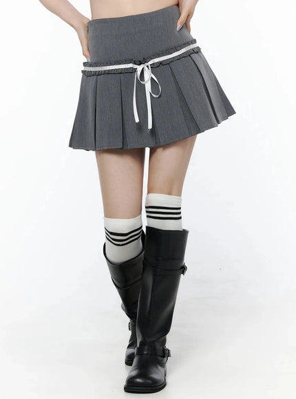 High-Waist Bow Pleated Skirt IL506 Dark gray front on model hands-on-hips, showing white ribbon bow and double ruffle trim detail with black knee-high boots