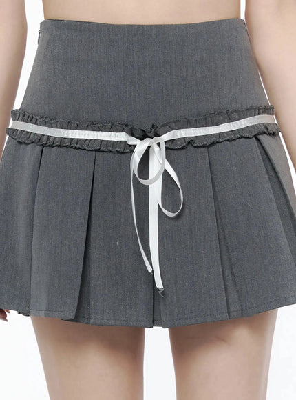 High-Waist Bow Pleated Skirt IL506 Dark gray close-up front detail showing double ruffle trim, white satin ribbon bow tie at waist, pleated fabric texture