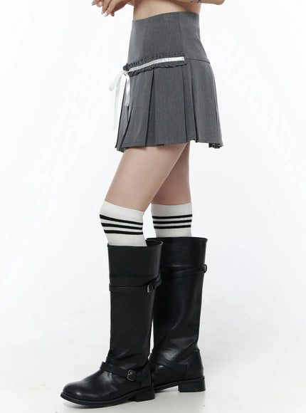 High-Waist Bow Pleated Skirt IL506 Dark gray side view on model showing high waistband, ruffle trim, white ribbon bow, and pleated hem with knee-high boots