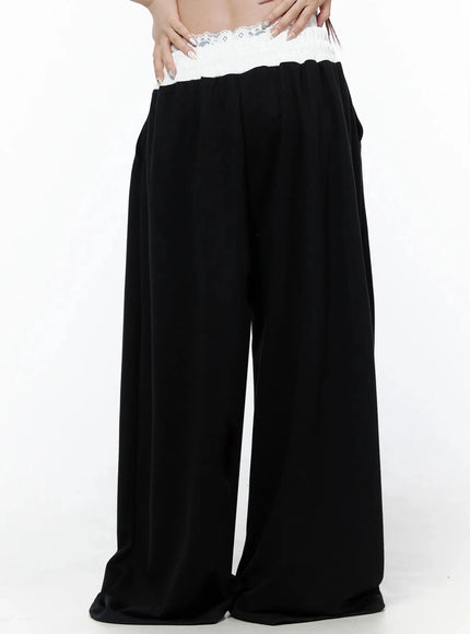 High-Waist Lace Wide Leg Sweatpants IL506 Black front model shot waist-down hands on waistband showing white lace trim and wide flowy leg without drawstring
