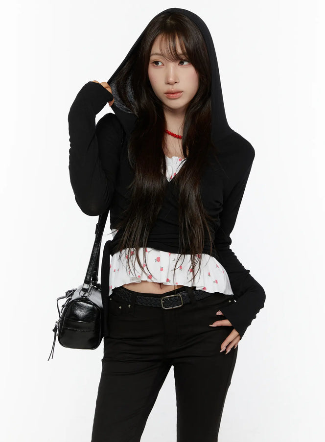 LEWKIN Hooded Wrap Crop Cardigan CL507 Black S/M front shot on model wearing hood up, adjusting hood with hand, styled with floral ruffle inner top and black jeans