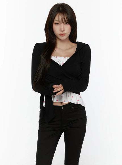 Hooded Wrap Crop Cardigan CL507 Black front shot on model arms crossed, V-wrap neckline with hooded detail, layered over white floral ruffle top, black jeans