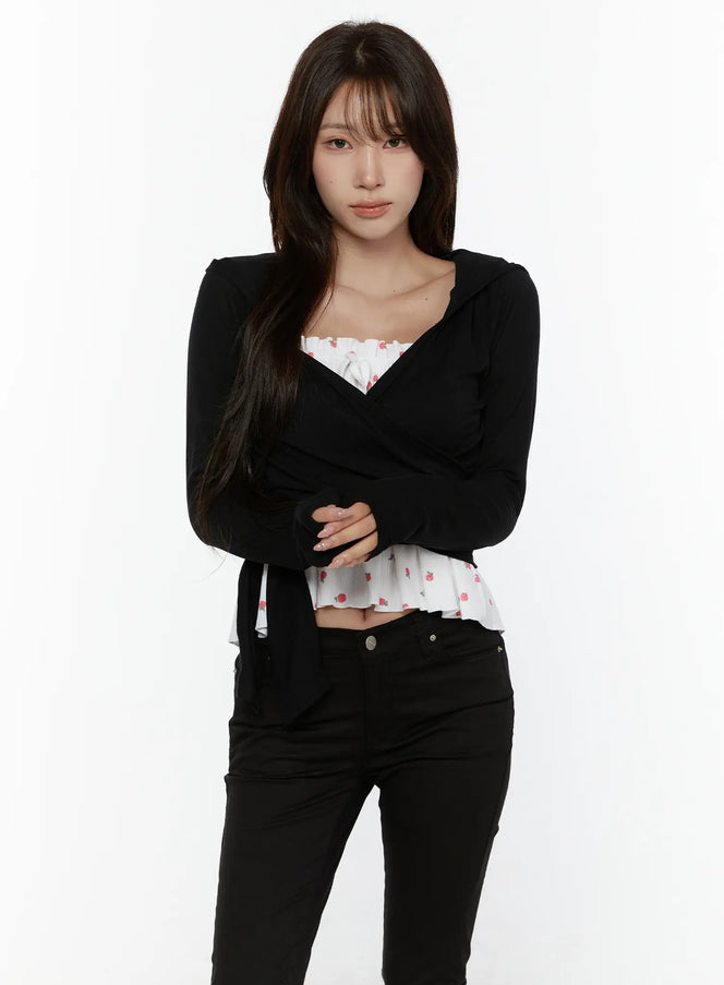 Hooded Wrap Crop Cardigan CL507 Black front shot on model arms crossed, V-wrap neckline with hooded detail, layered over white floral ruffle top, black jeans