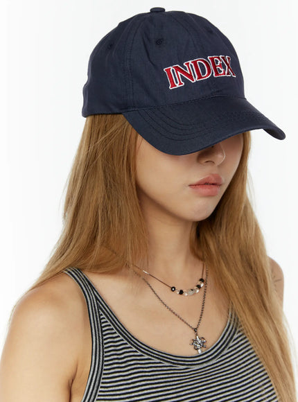 LEWKIN Index Cotton Ball Cap IL503 Navy front three-quarter view on model wearing striped tank top, red INDEX embroidery on crown, curved brim pulled low