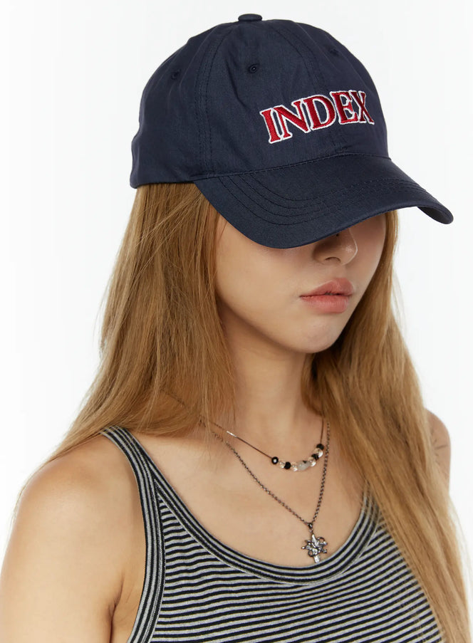 LEWKIN Index Cotton Ball Cap IL503 Navy front three-quarter view on model wearing striped tank top, red INDEX embroidery on crown, curved brim pulled low