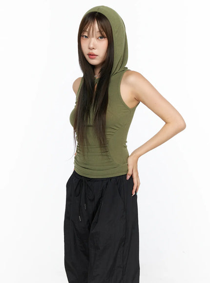 Keyhole Button Hooded Crop Sleeveless Top CL514 Dark green three-quarter model shot with hood up ruched waist styled with black parachute pants and brown shoulder bag