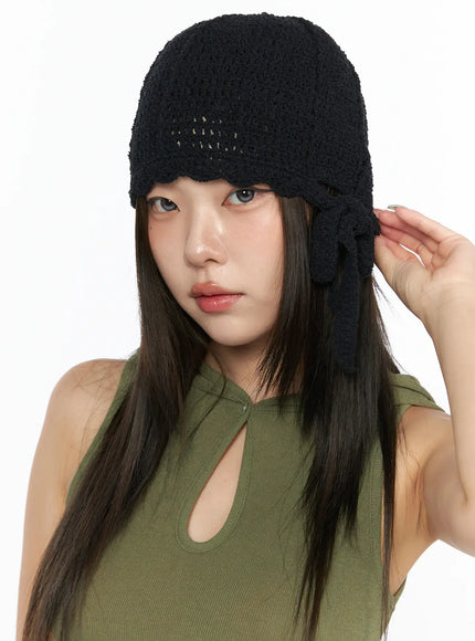 LEWKIN Knit Ribbon Beanie CL517 Black close-up front on model wearing green tank top, hand raised to side bow tie detail, open-knit crochet texture