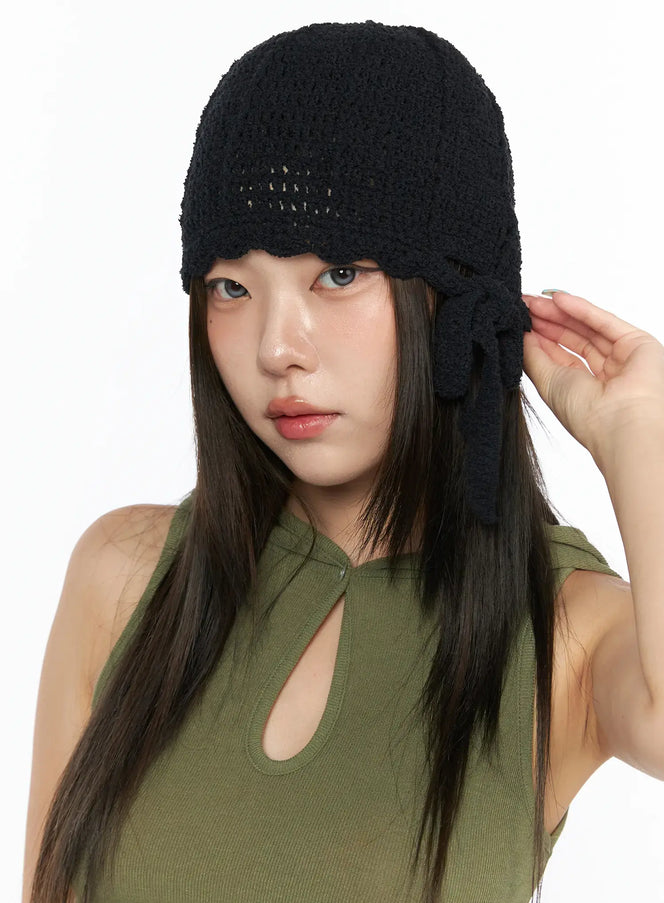 LEWKIN Knit Ribbon Beanie CL517 Black close-up front on model wearing green tank top, hand raised to side bow tie detail, open-knit crochet texture