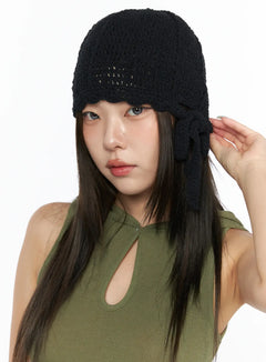 LEWKIN Knit Ribbon Beanie CL517 Black close-up front on model wearing green tank top, hand raised to side bow tie detail, open-knit crochet texture