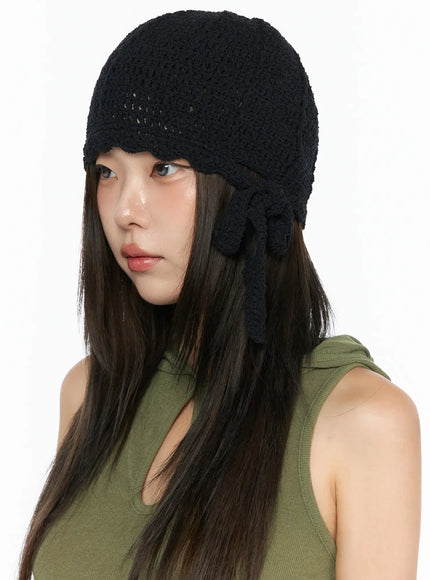 Knit Ribbon Beanie CL517 Black angled three-quarter view on model in green tank top, open-knit crochet dome with scalloped edge and bow tie detail at side