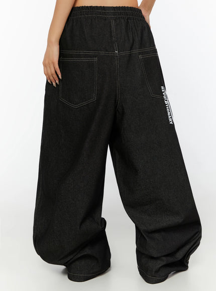 Kris Back Graphic Baggy Jeans IL524 Black back waist-down shot on model showing two back patch pockets REVOLUTIONARY text print and contrast white stitching details