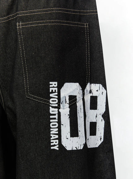Kris Back Graphic Baggy Jeans IL524 Black close-up detail of back leg showing REVOLUTIONARY 08 distressed white graphic print on dark denim with contrast stitching