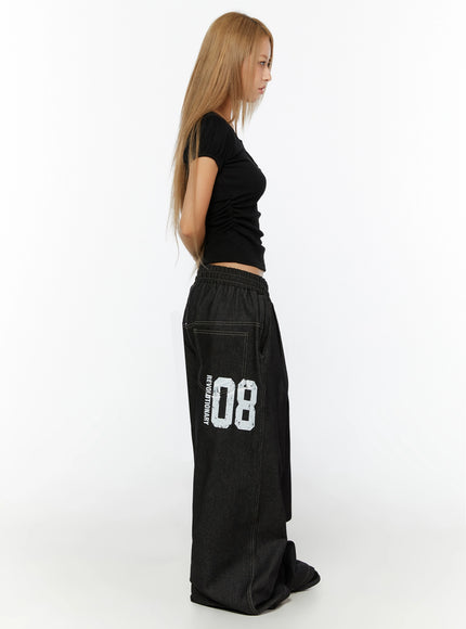 Kris Back Graphic Baggy Jeans IL524 Black side view on model styled with black crop top showing REVOLUTIONARY 08 white graphic print and wide-leg drape