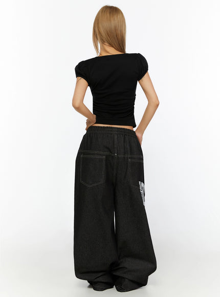 Kris Back Graphic Baggy Jeans IL524 Black back view on model styled with black crop top showing back patch pockets contrast stitching and partial REVOLUTIONARY print