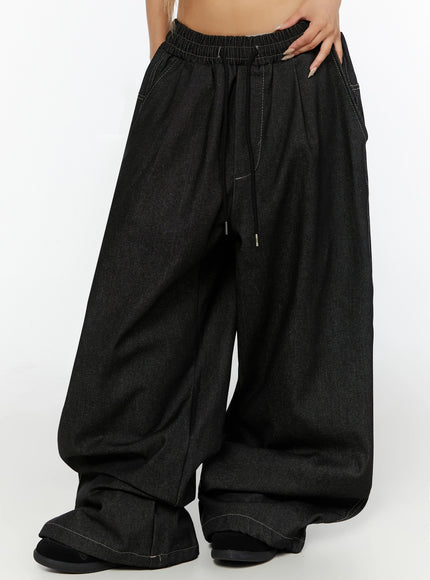 Kris Back Graphic Baggy Jeans IL524 Black front waist-down angled shot on model highlighting elastic drawstring waist pleats and wide denim leg with contrast topstitch