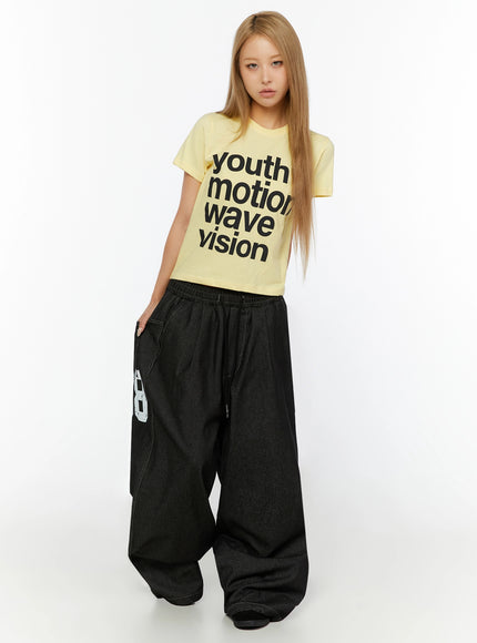 Kris Back Graphic Baggy Jeans IL524 Black front full-length view on model styled with yellow crop tee showing wide-leg baggy silhouette and side graphic print
