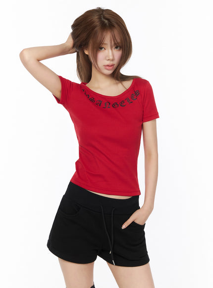 LA Graphic Round Neck Crop Top IL502 Red model front shot, hand on head pose, fitted ribbed crop top with gothic lettering, styled with black drawstring shorts