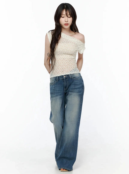 Lace Asymmetrical Off-Shoulder Top IL506 Light beige full-body front shot on model looking down one-shoulder lace top styled with wide-leg denim jeans