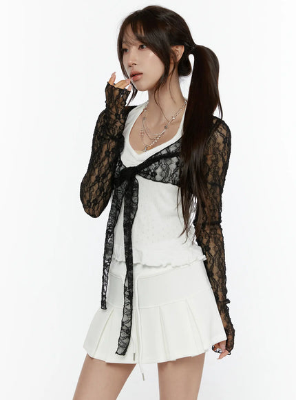 Lace Front-Tie Bolero CL507 Black front angled shot on model touching face, sheer black floral lace bolero with front tie over white ribbed top and white mini skirt