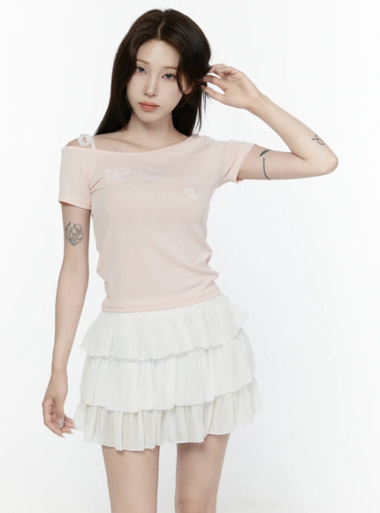Lace Off-Shoulder Top IL521 Pink front shot on model touching hair showing fitted ribbed knit with lace off-shoulder strap and butterfly script print