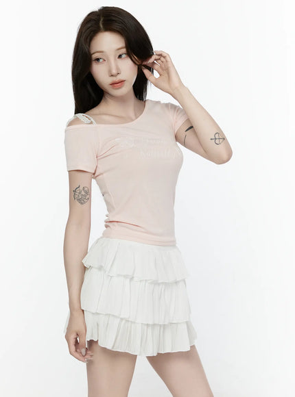 Lace Off-Shoulder Top IL521 Pink three-quarter front shot on model touching hair showing asymmetric neckline and butterfly script graphic print