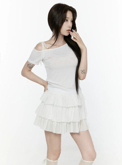 Lace Off-Shoulder Top IL521 White three-quarter side shot on model hand near face showing off-shoulder lace strap and butterfly script on sheer ribbed knit