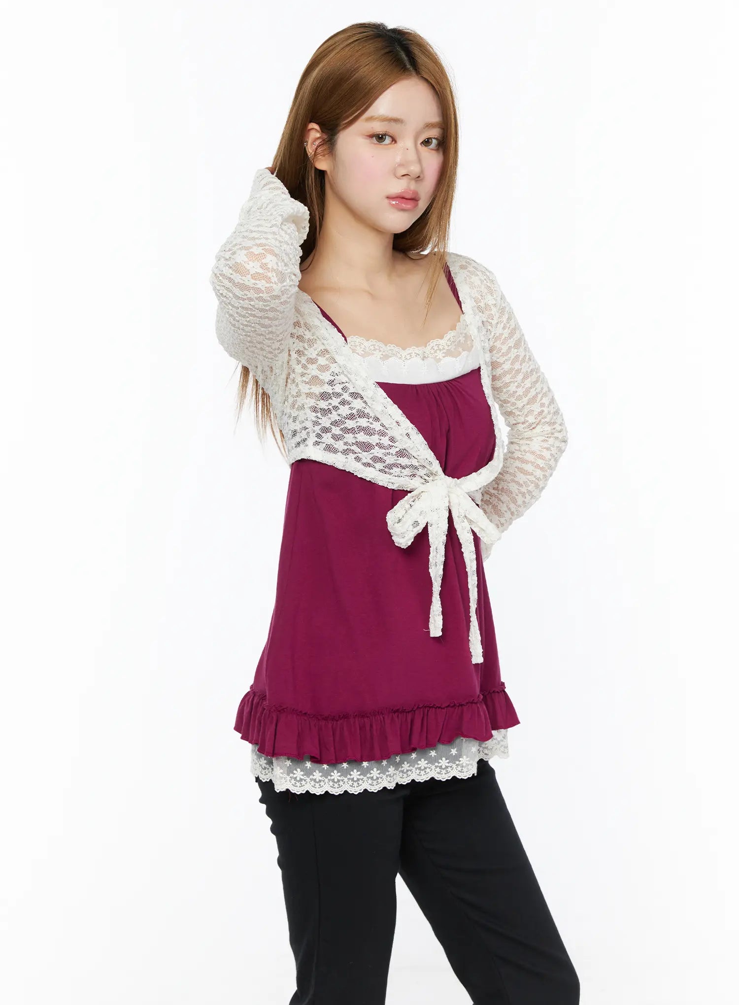 Lace Sheer Crop Cardigan CL502 White three-quarter front shot on model touching hair, lace tie bow detail visible over magenta cami with black pants