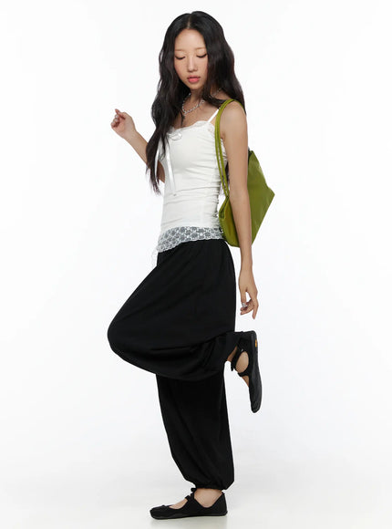 Lace Trim Cami Top CL513 White full-body side view on model with dynamic pose, green shoulder bag, lace hem peeking over black pants, ribbed fitted silhouette