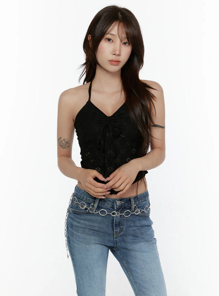 Lace Trim Halter Neck Cami CL508 Black front model shot standing with hands clasped showing eyelet lace crop top with center ribbon tie styled with blue jeans and chain belt