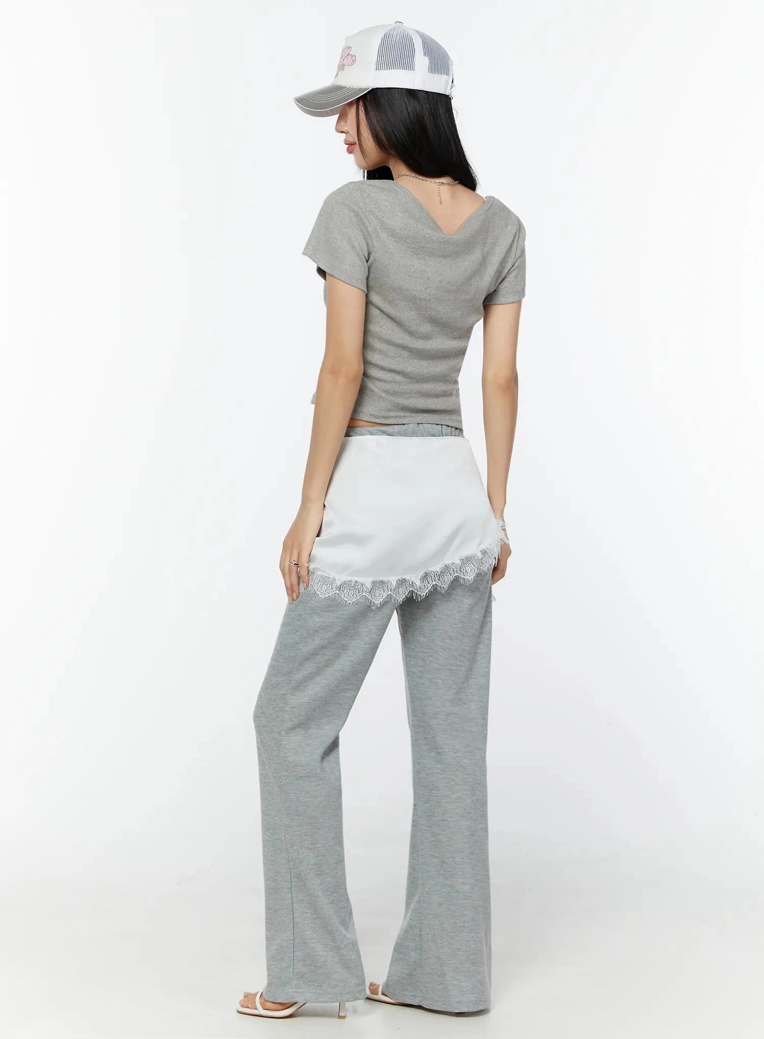 Lace Trim Satin Layering Skirt IU524 White back full-body shot on model wearing cap and crop tee showing white satin wrap panel with lace trim over gray flare pants