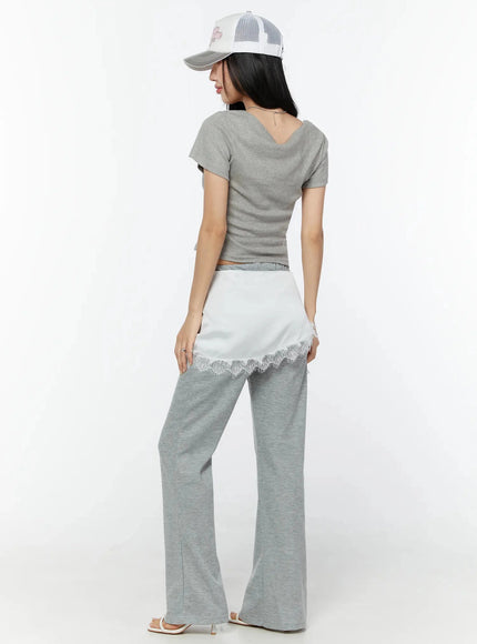 Lace Trim Satin Layering Skirt IU524 White back full-body shot on model wearing cap and crop tee showing white satin wrap panel with lace trim over gray flare pants