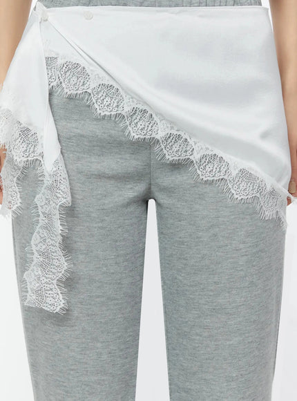 LEWKIN Lace Trim Satin Layering Skirt IU524 White close-up detail on model showing asymmetric wrap silhouette with scalloped lace trim edging over gray flare pants