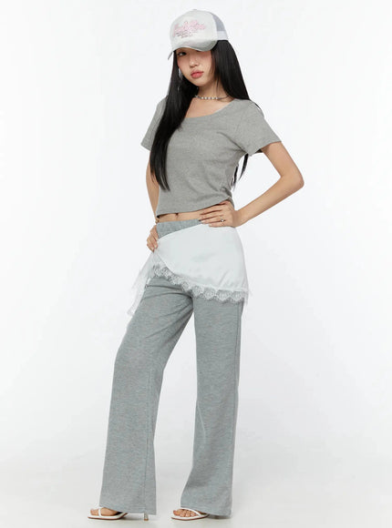 Lace Trim Satin Layering Skirt IU524 White three-quarter front shot on model with hand on hip showing diagonal lace-trimmed hem layered over gray wide-leg pants