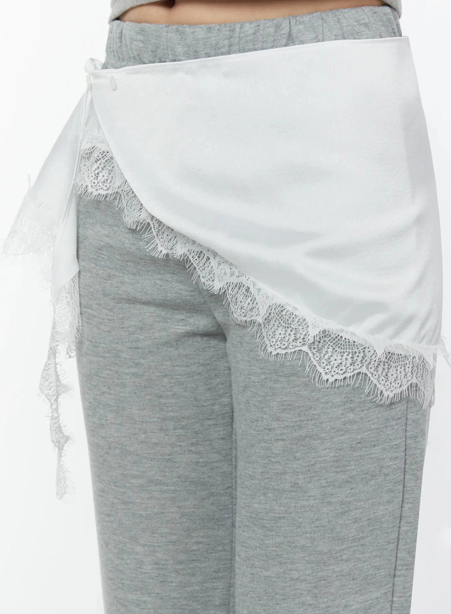 Lace Trim Satin Layering Skirt IU524 White close-up front detail on model highlighting asymmetric wrap drape and floral scalloped lace trim over gray pants