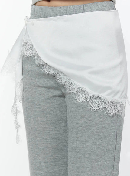 Lace Trim Satin Layering Skirt IU524 White close-up front detail on model highlighting asymmetric wrap drape and floral scalloped lace trim over gray pants
