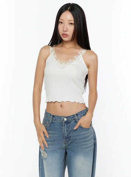 Lace Trim Tank CU526 White front view on model, floral lace V-neckline, ribbed knit crop tank with lettuce hem, hands in pockets, styled with blue jeans