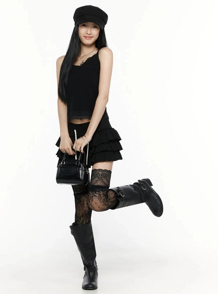 Lace Trim Tank Top IL516 Black front shot on model one leg raised, lace V-neckline and hem trim, styled with black ruffle mini skirt, lace thigh-highs, boots and cap