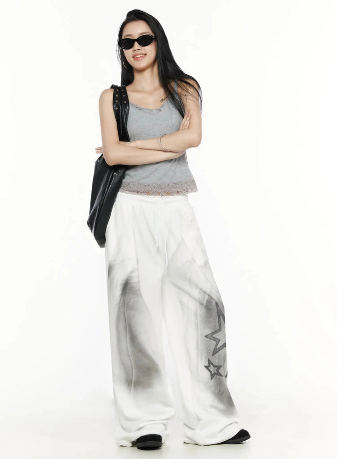 Lace Trim Tank Top IL516 Gray front shot on model arms crossed, lace hem trim, ribbed texture, styled with white star-print wide-leg sweatpants and sunglasses
