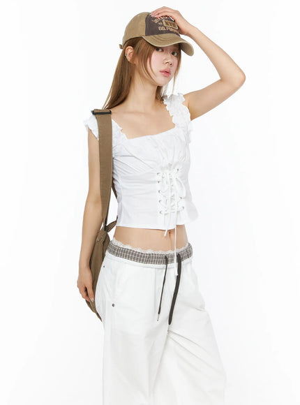 LEWKIN Lace-Up Corset Blouse Top CL502 White S/M angled front shot on model wearing cap and crossbody bag with ruched ruffle straps and lace-up corset detail