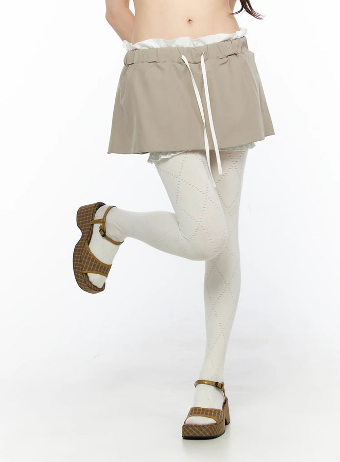 LEWKIN Layered Low-Rise Mini Skirt CL523 Beige close-up front model shot showing drawstring waist ruffle lining and flared hem with white patterned tights