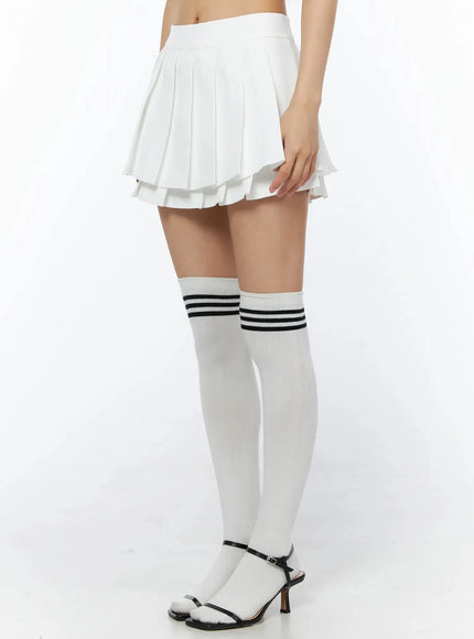 Layered Pleated Skirt IL509 White side close-up on model highlighting double-layer pleated hem detail and over-the-knee striped socks with black sandals