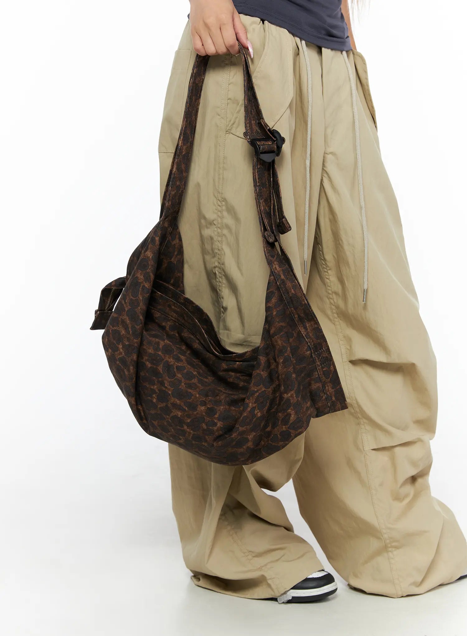 Leopard Print Sling Shoulder Bag CU524 Brown lower-body detail shot model holding bag by handles against beige cargo pants showing buckle and strap