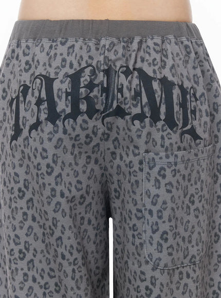Leopard Print Wide-Leg Sweatpants IU525 Dark gray close-up back detail shot showing large gothic-script TAKEME print and patch pocket on leopard fabric