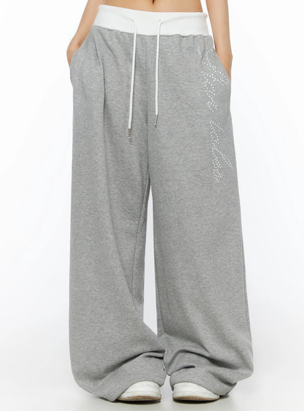 Lettering Contrast Waist Sweatpants IL515 Gray front mid-shot on model with hands in pockets showing white contrast waistband, star-dot graphic, and pooling wide-leg hem